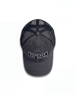 Black washed trucker hat with embroidered Embrace The Grind patch — front view